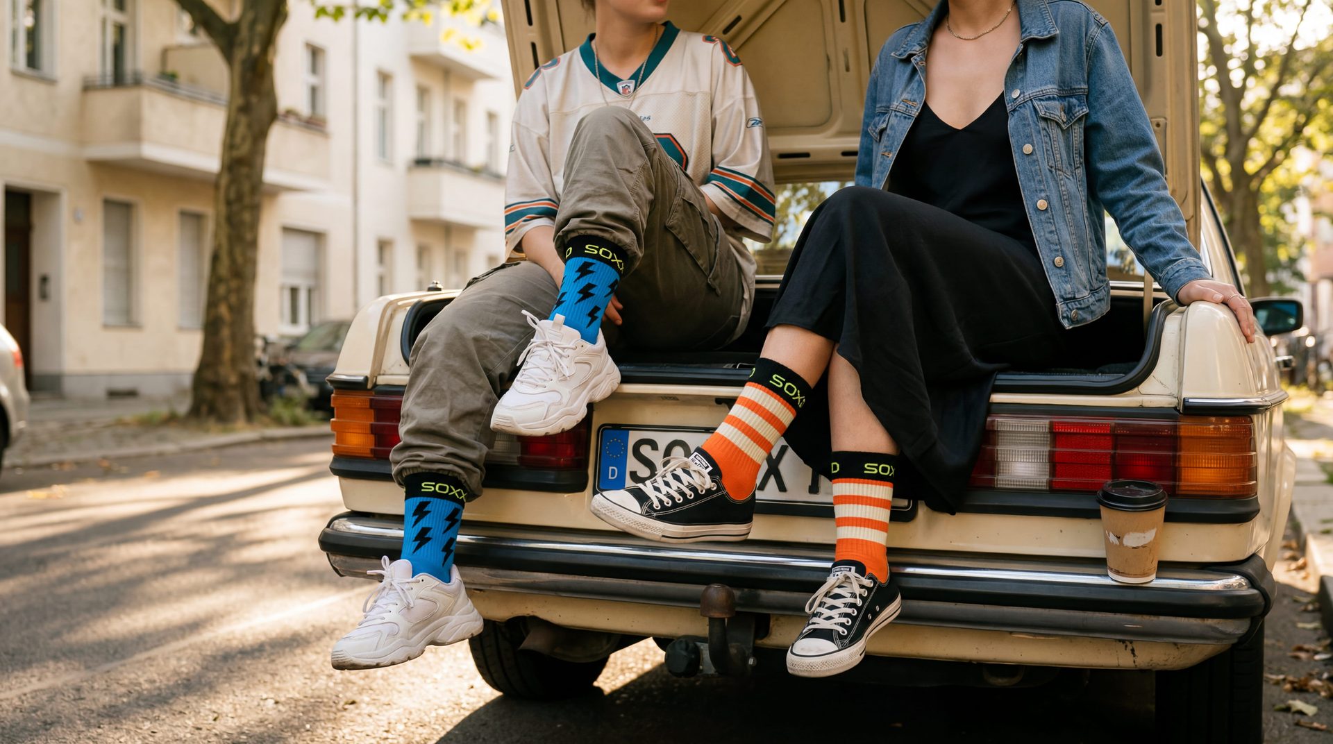 Two friends sitting on a vintage car tailgate in Berlin, wearing SOXXD socks.
