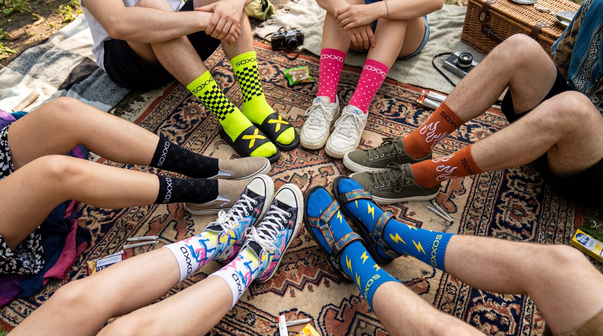 Group of friends in a circle showing off pink, neon, and checkerboard SOXXD socks on a Berlin rug.